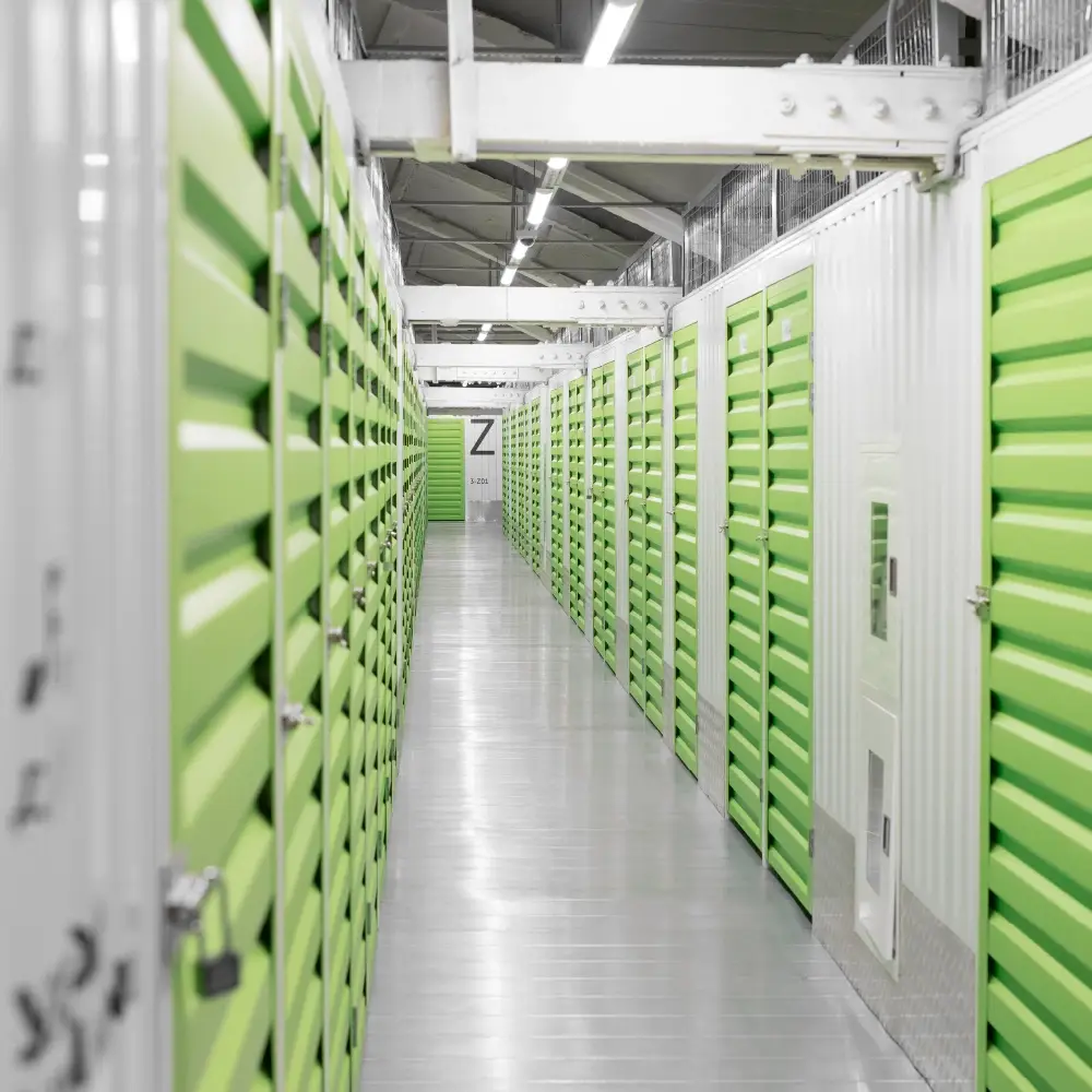 A clean, brightly lit storage facility hallway with green doors on both sides.