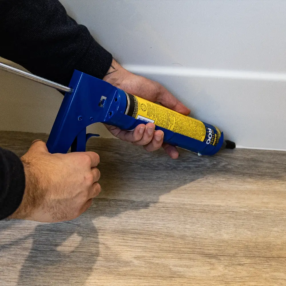 An employee uses a caulking gun to seal the edges of a bathtub, demonstrating precision and professionalism.