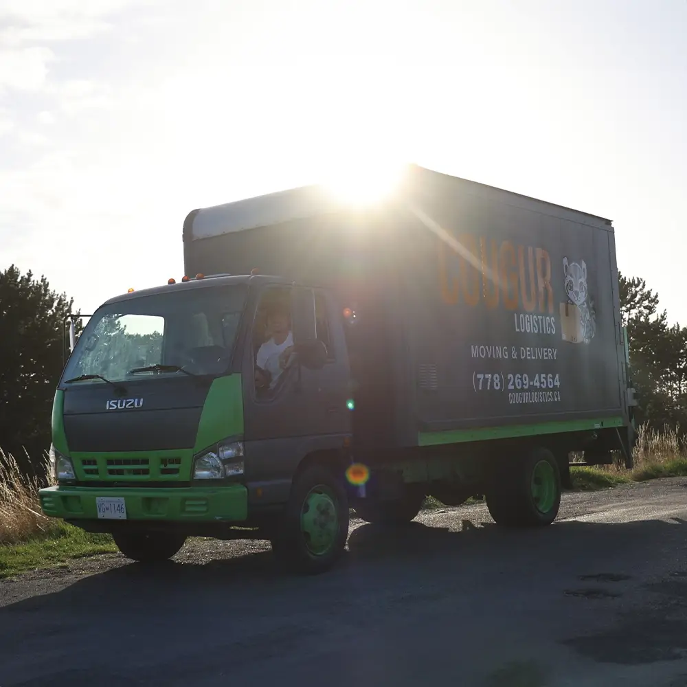 The founder of Cougur Logistics sitting in the driver’s seat of a truck, with a vibrant sunset in the background.