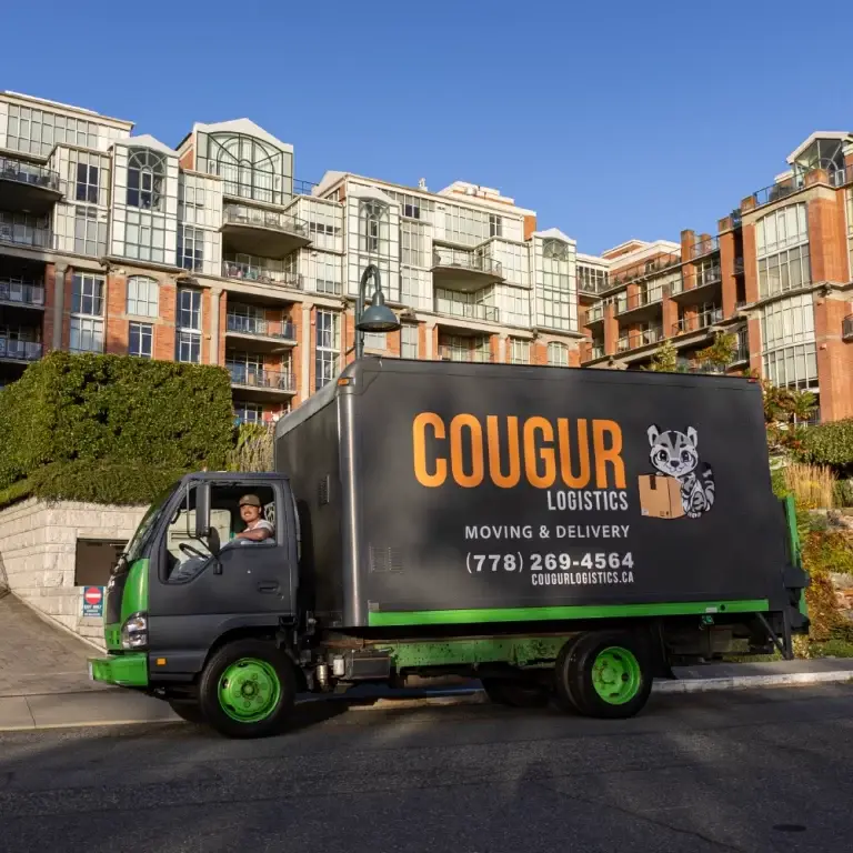 A green and black Cougur Logistics delivery truck parked near modern residential buildings on a sunny day.