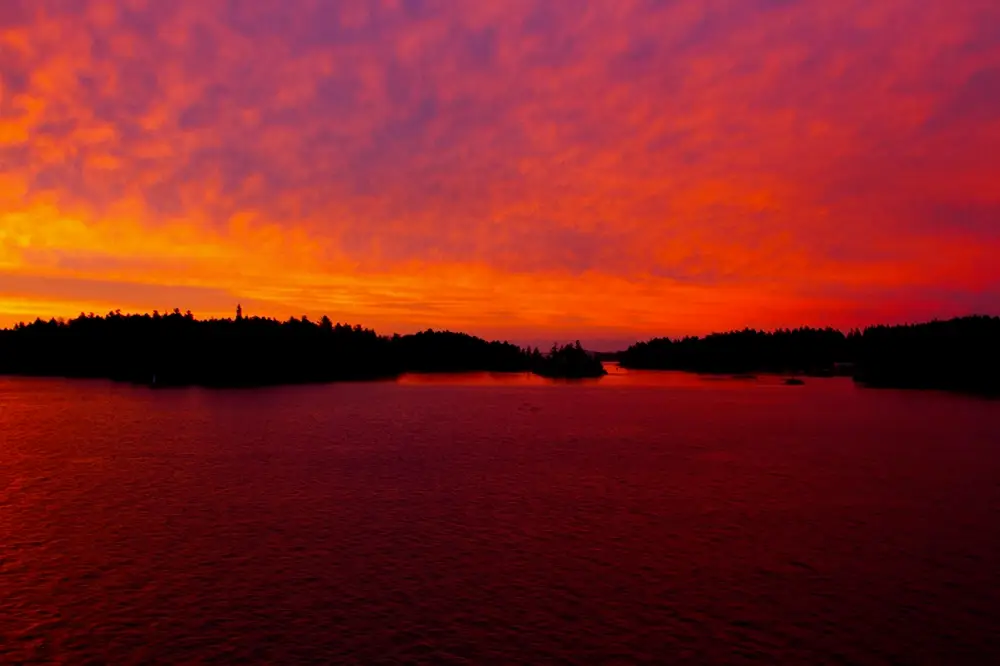 Stunning sunset over Victoria's Inner Harbour with bright red skies reflecting on the ocean."