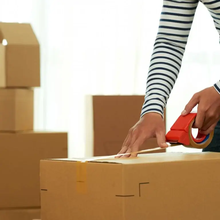 An employee seals a cardboard box with packing tape, ensuring it is securely closed for transport.