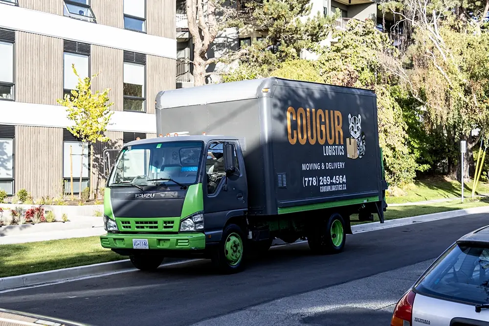 Cougur Logistics moving truck parked in downtown Victoria in front of a modern apartment building.